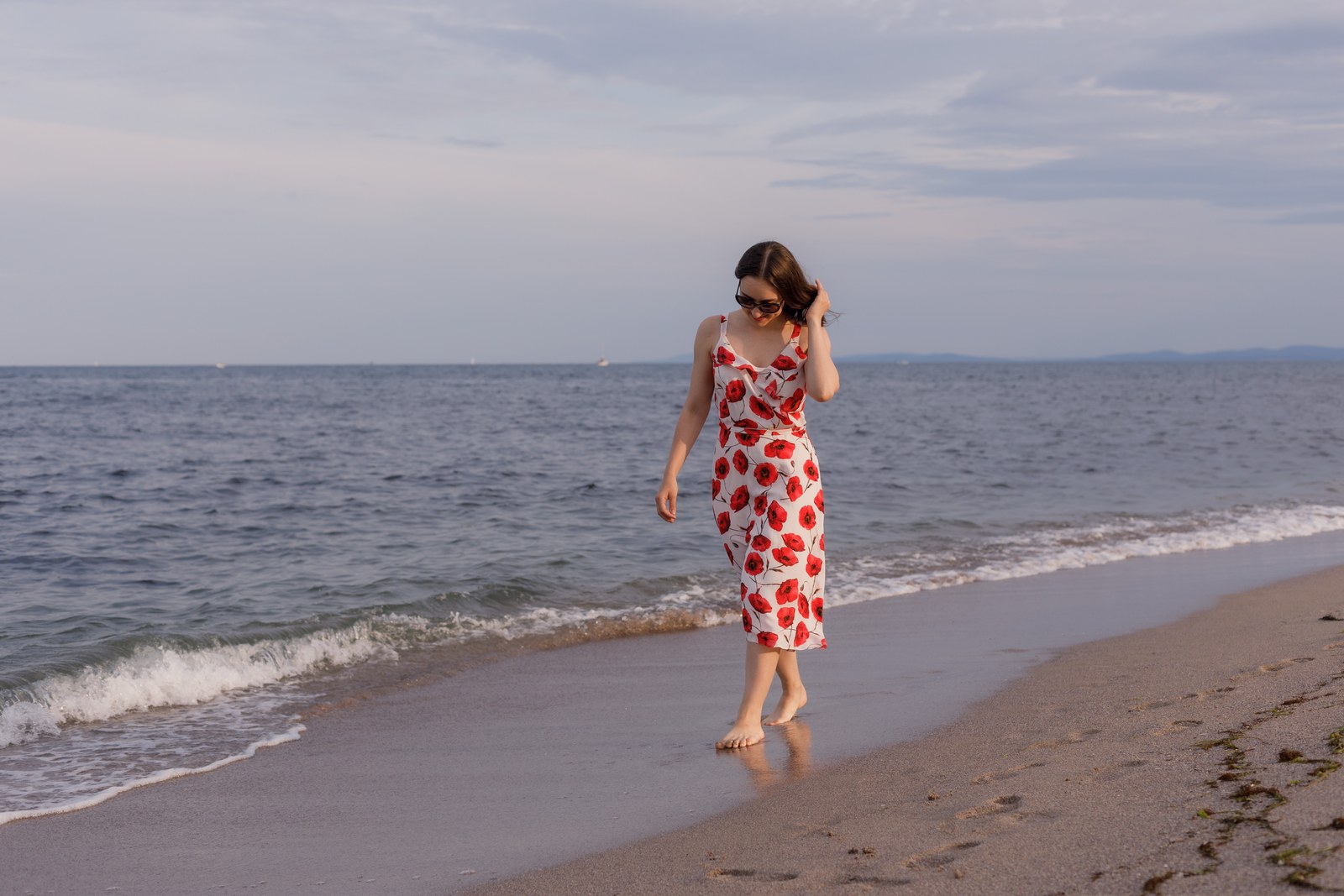 Woman walking along the shoreline in a poppy-print dress